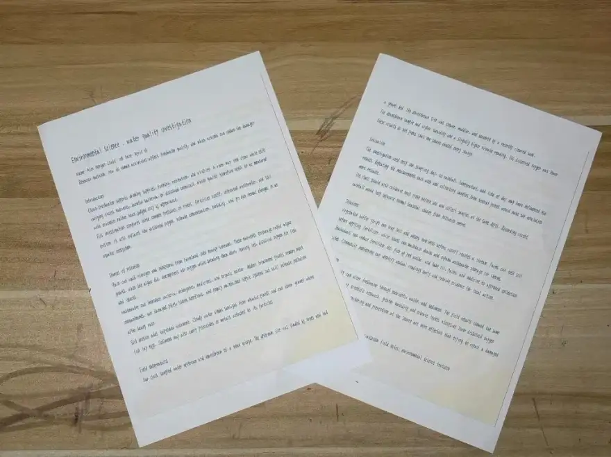 Two printed pages of an environmental science assignment mockup laid on a wooden desk